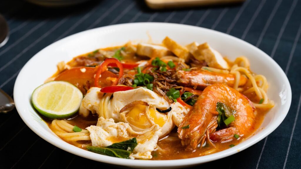 Mee Bandung, a tantalizing Malaysian dish, boasts a robust tomato-infused broth with a spicy and tangy kick, complementing the flavorful noodles for a satisfying culinary experience.